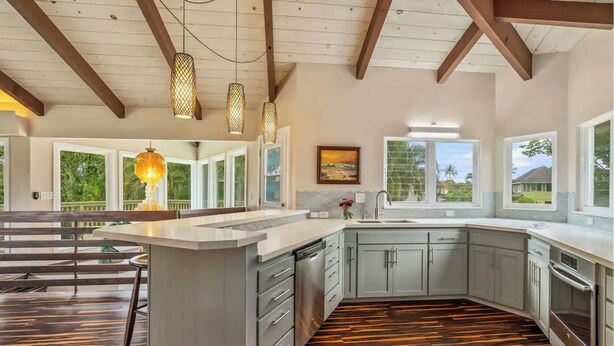 A modern kitchen with a large island, wooden flooring, and large windows offering views of the outdoors.