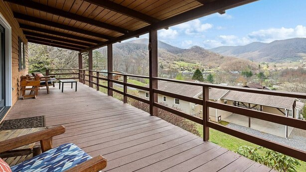 Un terrazzo in legno con ringhiera, posti a sedere all'aperto e vista su una valle montuosa.