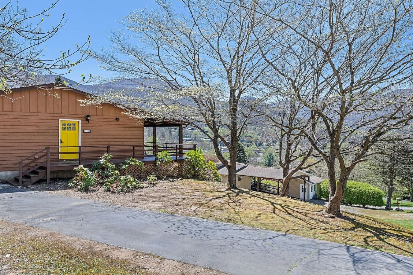 A rustic wooden cabin with a yellow door, a covered porch, and a view of mountains in the background.