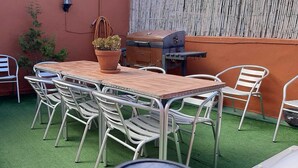 Eine Terrasse im Freien mit einem Holztisch, Metallstühlen, einem Grill und einem Blumentopf.