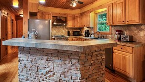 A kitchen with wooden cabinets, a stone island, and pendant lighting. - Falcon’s Nest-Spacious w/Spectacular Views!Hot Tub (Maggie Valley)