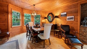 A cozy cabin interior with a wooden dining table, chairs, and a fireplace. - Falcon’s Nest-Spacious w/Spectacular Views!Hot Tub (Maggie Valley)