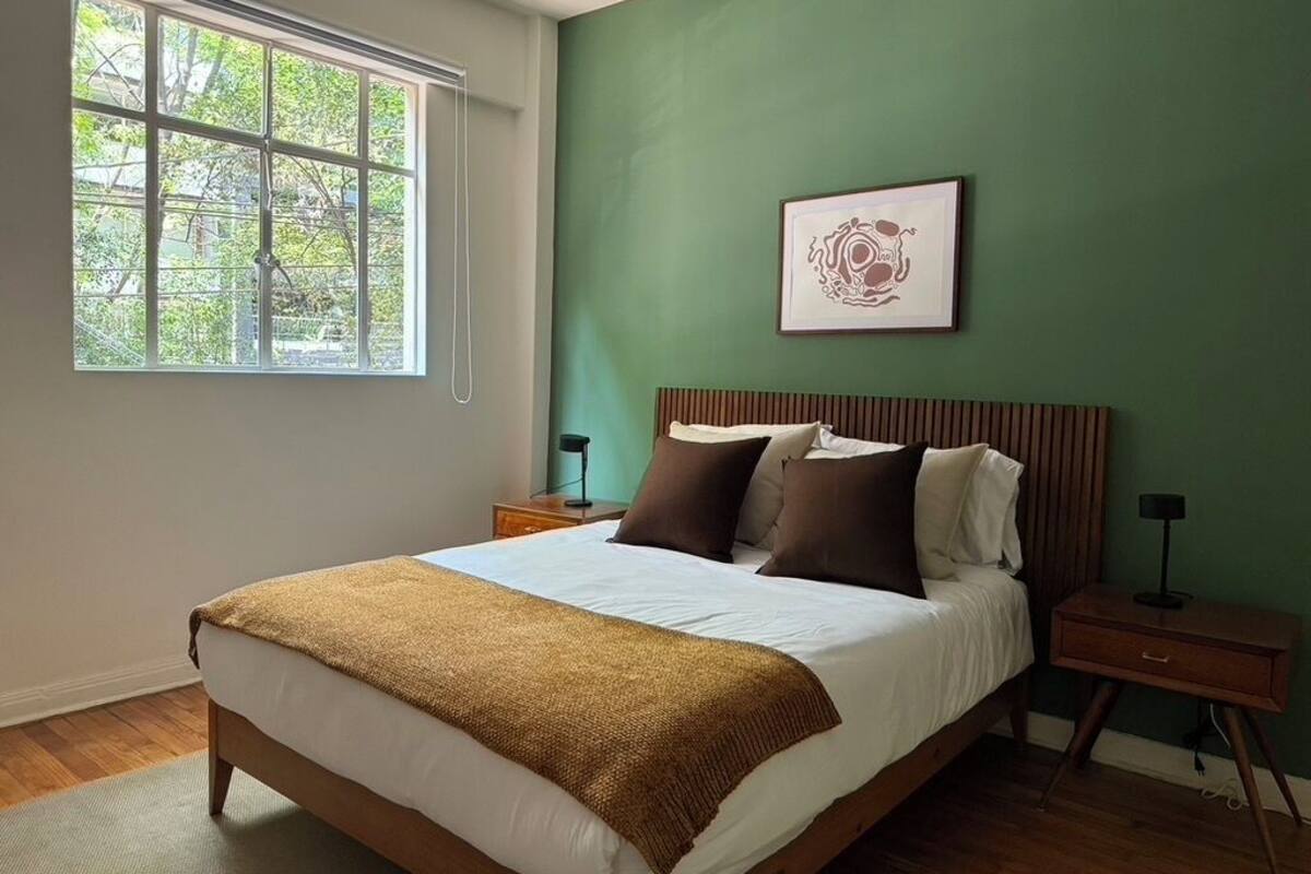Quarto com uma cama grande, uma janela, uma parede verde e um quadro emoldurado.