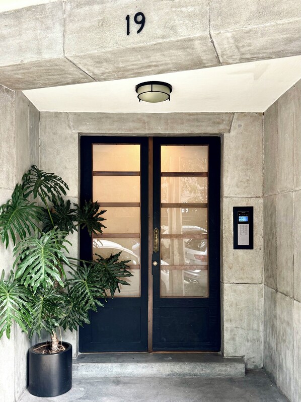 Entrada de um edifício com porta dupla preta, um vaso de planta e um teclado digital na parede.