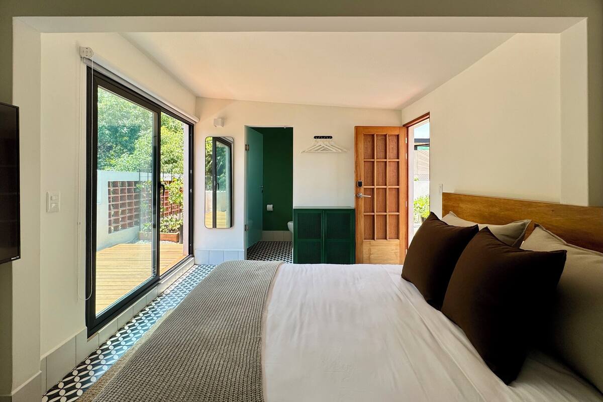 Quarto de hotel moderno com uma cama grande, televisão e porta de vidro deslizante para uma varanda.