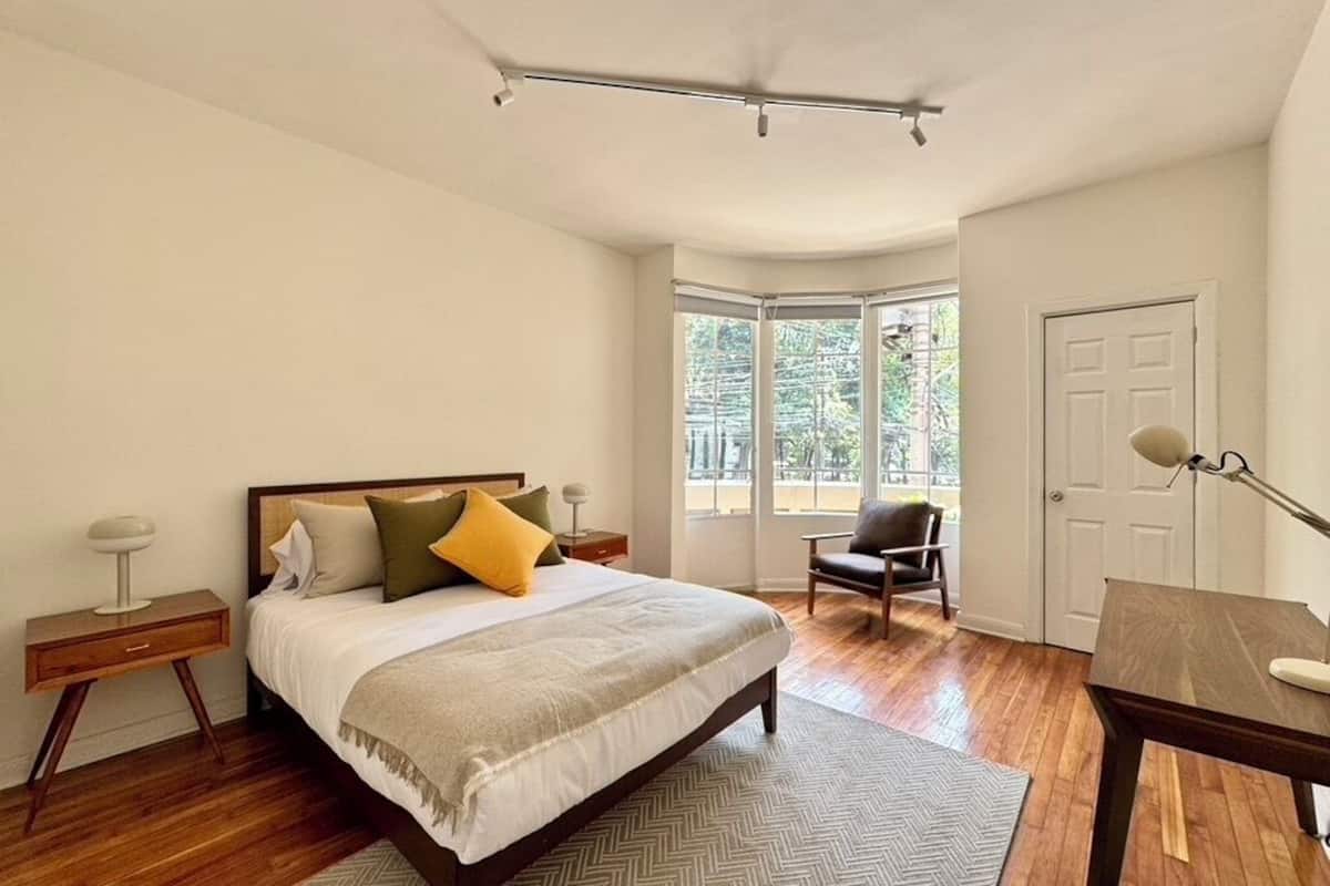 Quarto com cama, cadeira, escrivaninha e janela.
