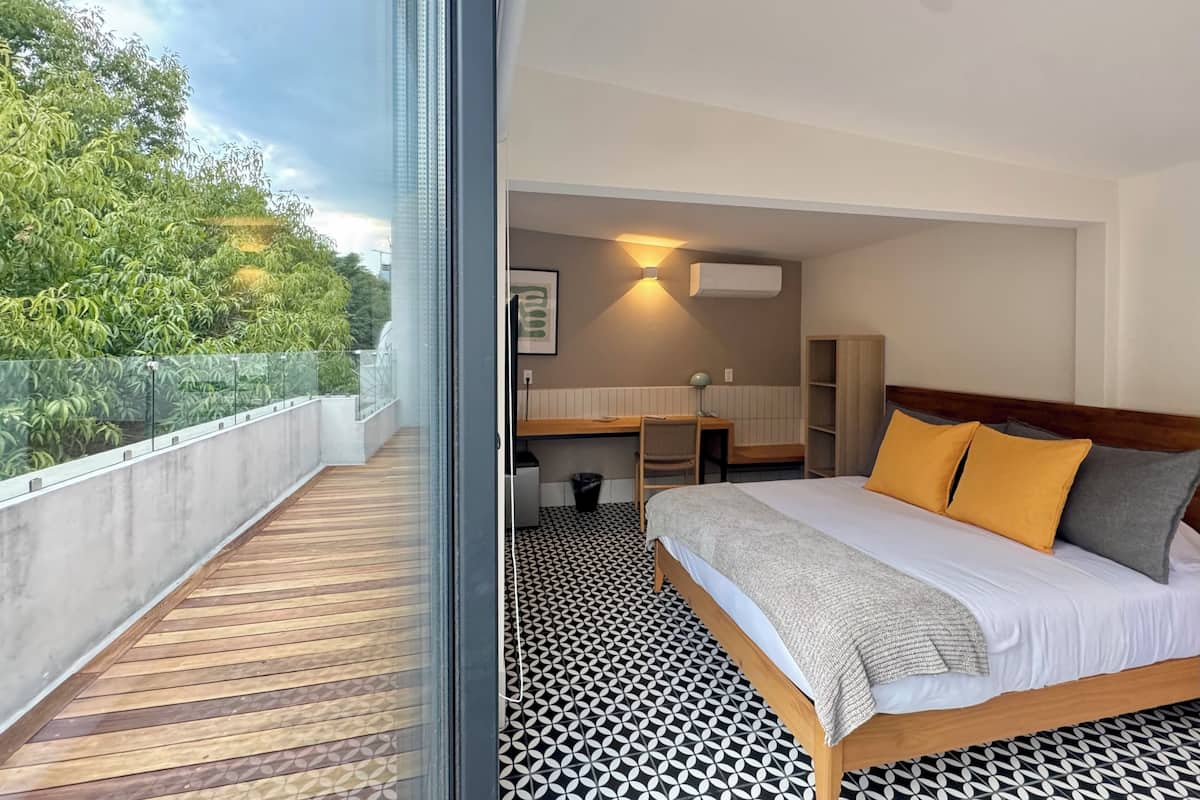 Quarto de hotel com cama, secretária e banheiro. Possui uma varanda com vista para árvores.