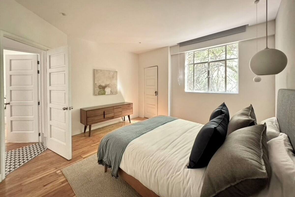Quarto com cama, mesa de cabeceira, penteadeira, janela e porta.
