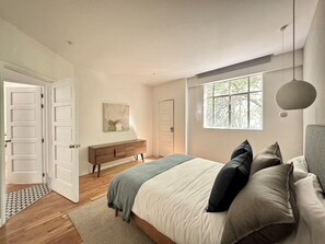 Quarto com cama, mesa de cabeceira, penteadeira, janela e porta.