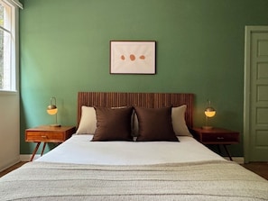 Ein Schlafzimmer mit einem Bett, zwei Nachttischen, einem Wandbild und einer Tür.