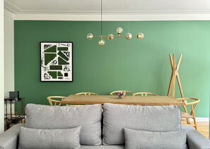 Ein Essbereich mit grüner Wand, einem Holztisch und einem grauen Sofa.