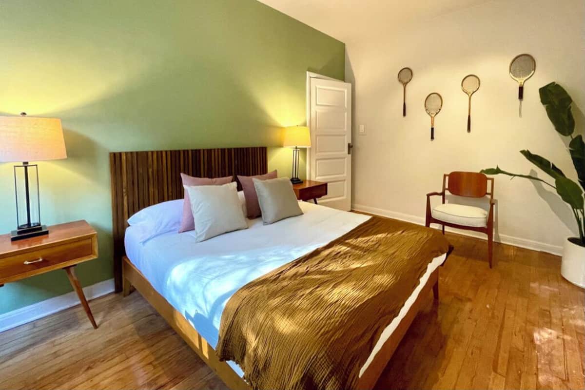Quarto bem arrumado com cama, mesas de cabeceira, uma cadeira e raquetes de badminton fixadas na parede.