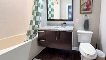 A bathroom with a bathtub, a sink with a granite countertop, a toilet, and a shower curtain.
