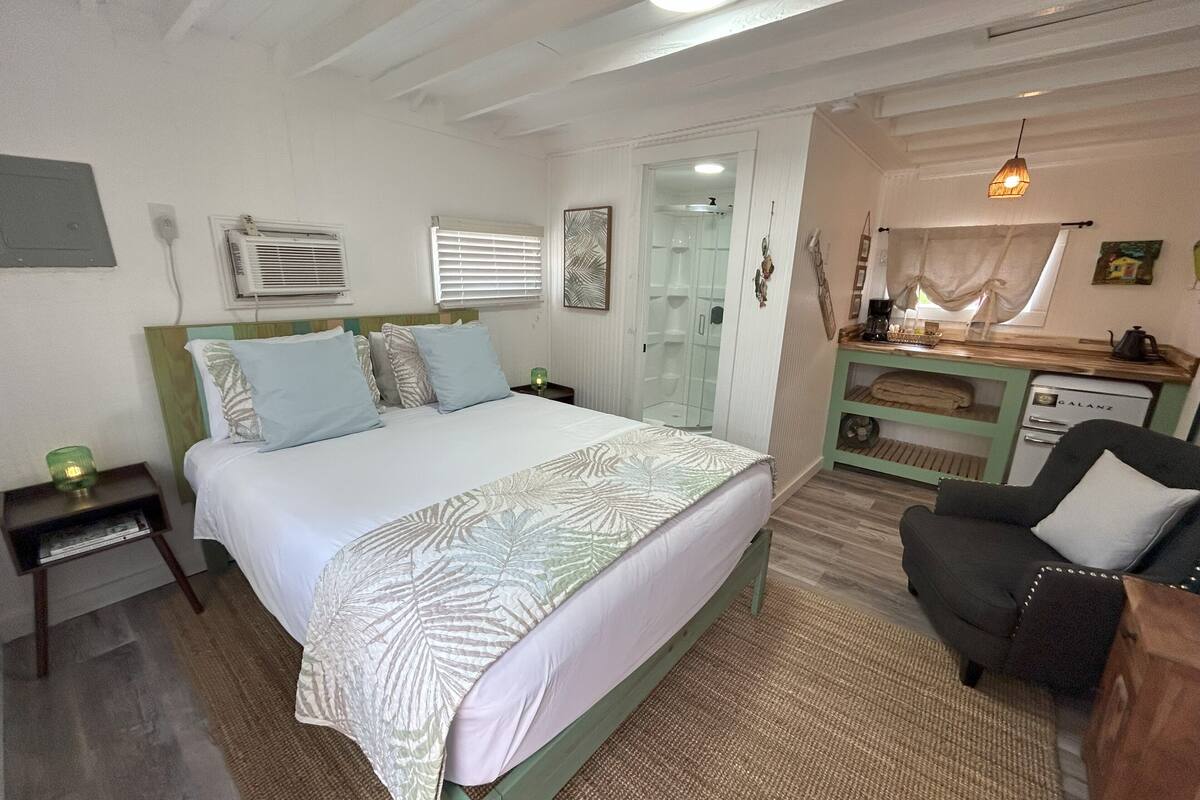 Un dormitorio con cama, mesitas de noche, un escritorio, una silla, una lámpara colgante y una zona de ducha.