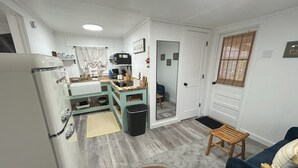 A compact kitchen with a refrigerator, sink, and wooden counter. There is a small seating area with a chair and a table. - Old Florida Fish Camp (Cedar Key)