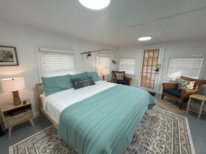 A bedroom with a bed, a chair, a nightstand, a lamp, and a window with blinds. - Old Florida Fish Camp (Cedar Key)