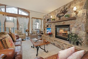 A cozy living room with a stone fireplace, leather sofas, and a large window with curtains. - Beautiful 4 Bedroom Condo with pool and hot tub access. 150 yards to Gondola (Vail)