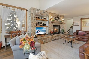 A cozy living room with a stone fireplace, a television, and comfortable seating. - Beautiful 4 Bedroom Condo with pool and hot tub access. 150 yards to Gondola (Vail)