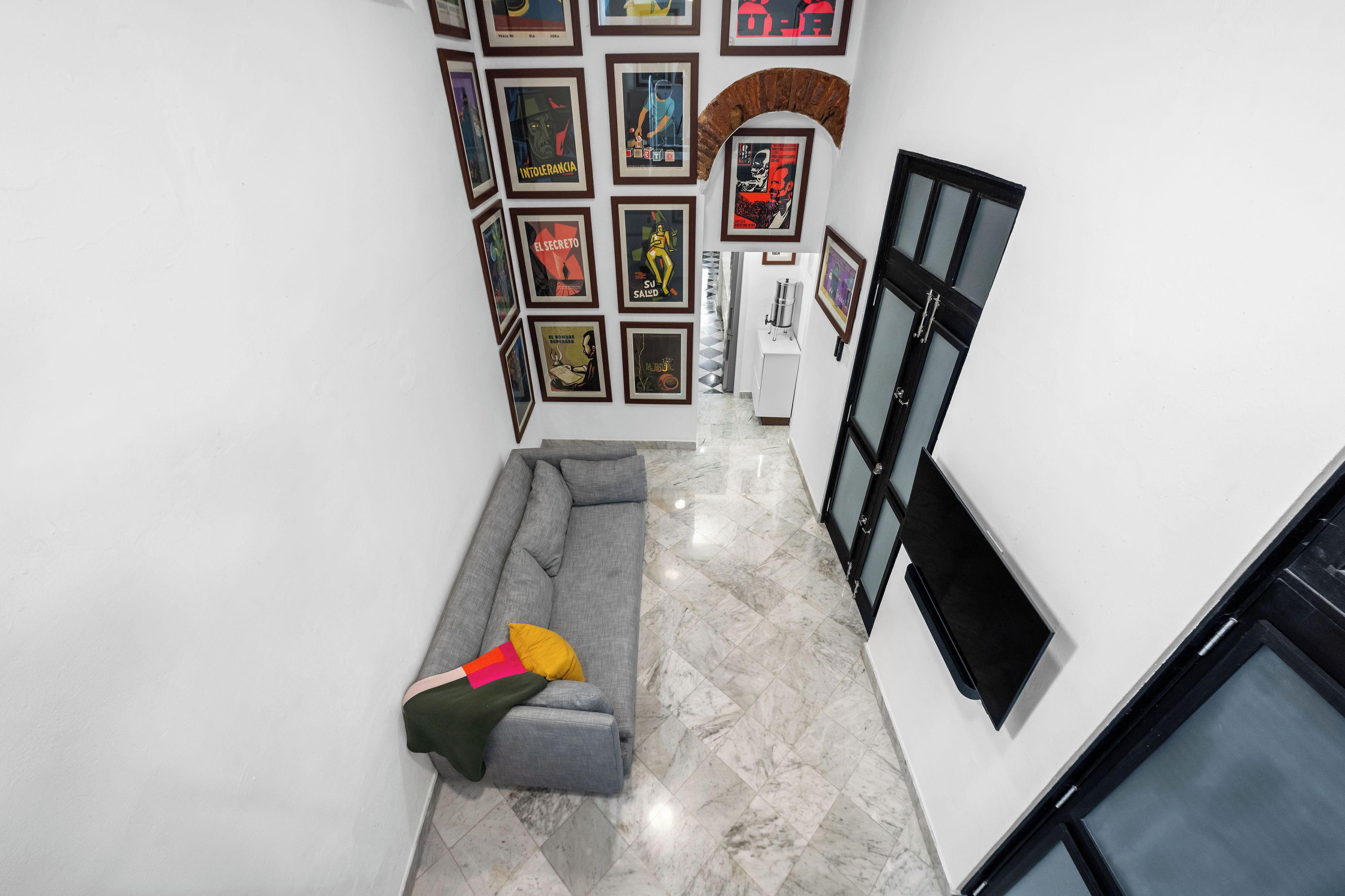 Un couloir avec un canapé gris, une armoire blanche et un mur décoré de tableaux encadrés.