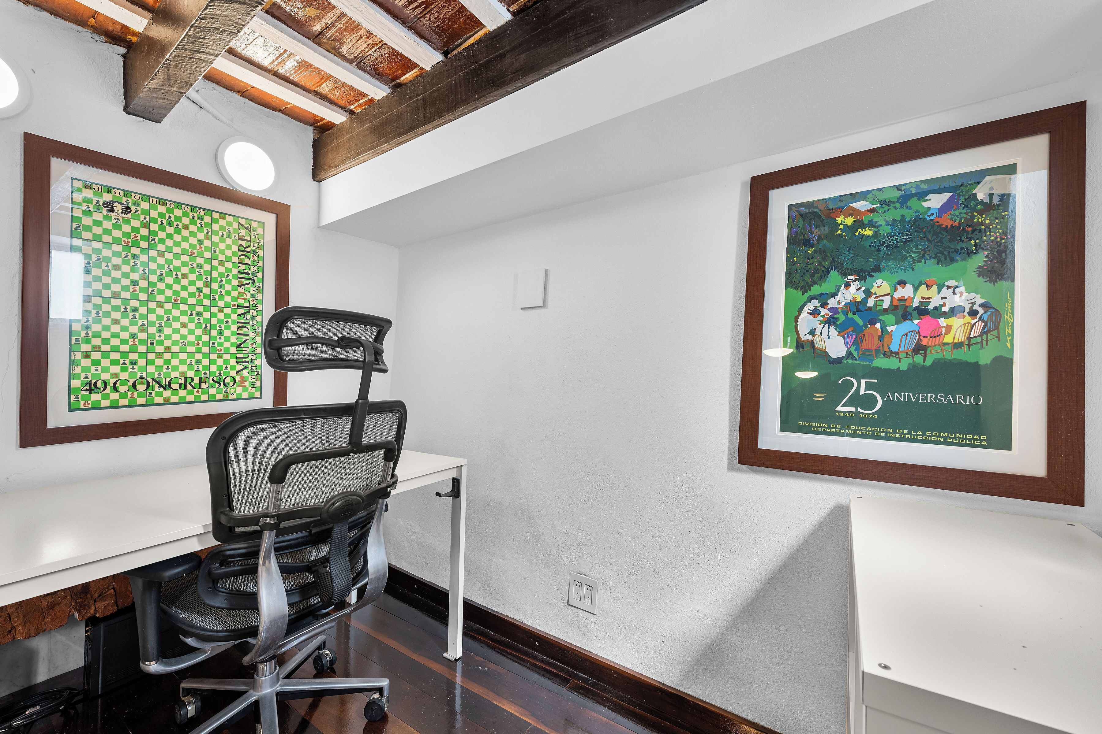 Una sala de conferencias con un tablero de ajedrez, un cartel enmarcado y un escritorio blanco con una silla.