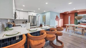 A modern kitchen with white cabinets, a stainless steel refrigerator, and a dining area with wooden tables and chairs. - Game Room, Cinema & Fire Pit Backyard (Denver)
