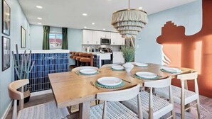 A dining area with a wooden table set for four, white chairs, and a hanging light fixture. - Game Room, Cinema & Fire Pit Backyard (Denver)