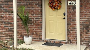 Una casa de ladrillo con una puerta amarilla, un cartel con el número 410, un adorno floral y una planta en maceta.