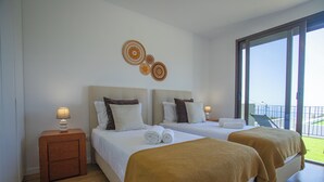 A hotel room with two beds, a small wooden nightstand, and a large window offering a view of the outdoors. - Dori’s Modern Home w/Pool & Sea & Mountain Views — 15 Min to City Center (Funchal)