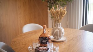A round wooden table with a bottle of liquor, two glasses, and a decorative plate. - Dori’s Modern Home w/Pool & Sea & Mountain Views — 15 Min to City Center (Funchal)