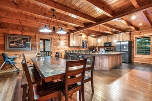 A spacious wooden cabin with a large dining table, kitchen area, and a view of the outdoors. - Timber Sky Lodge! Elevator/Pool/Theater | Sleep 27 (Sevierville)