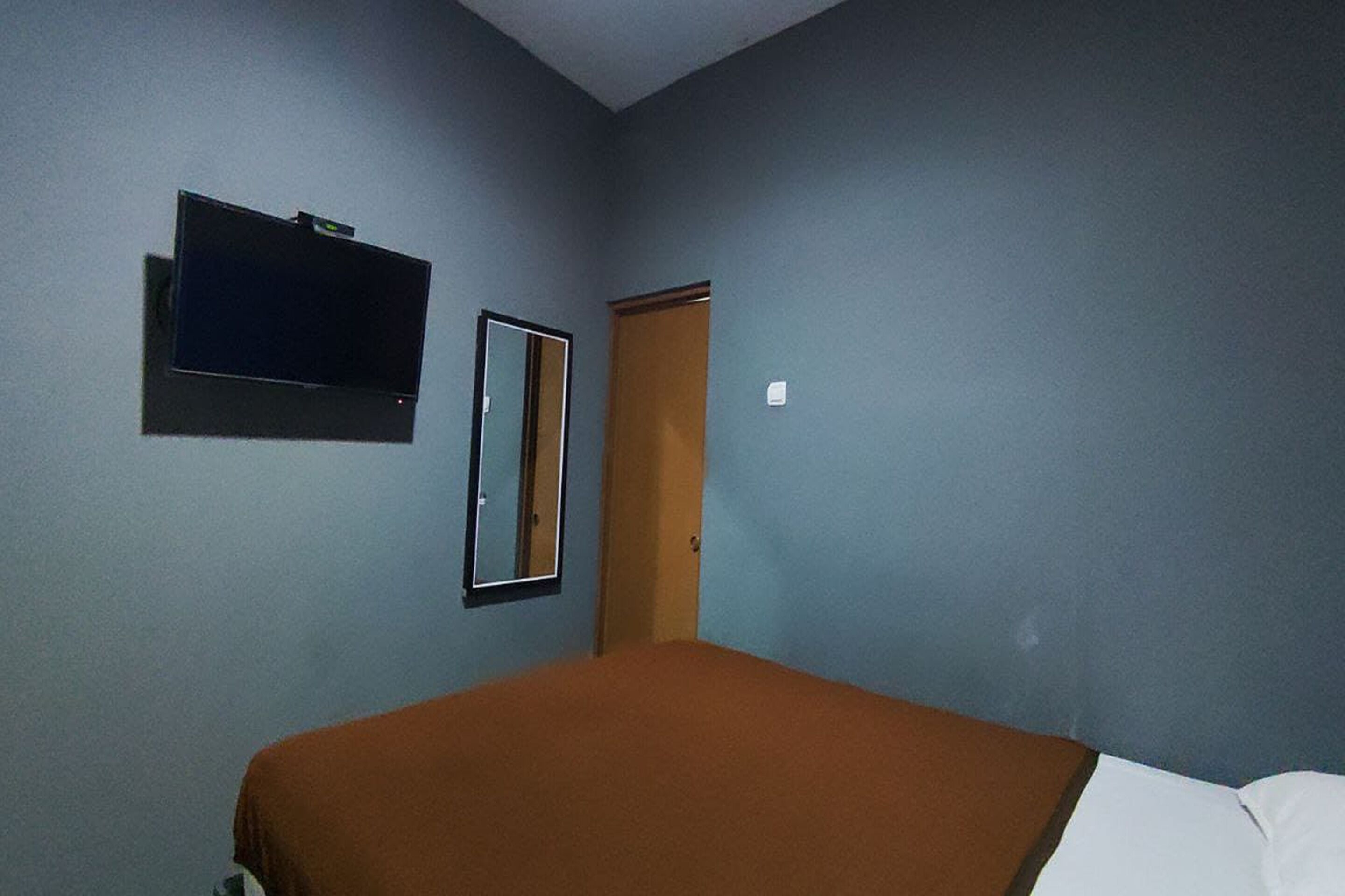 Ein Zimmer mit einem Bett, einem an der Wand befestigten Fernseher und einer Tür.