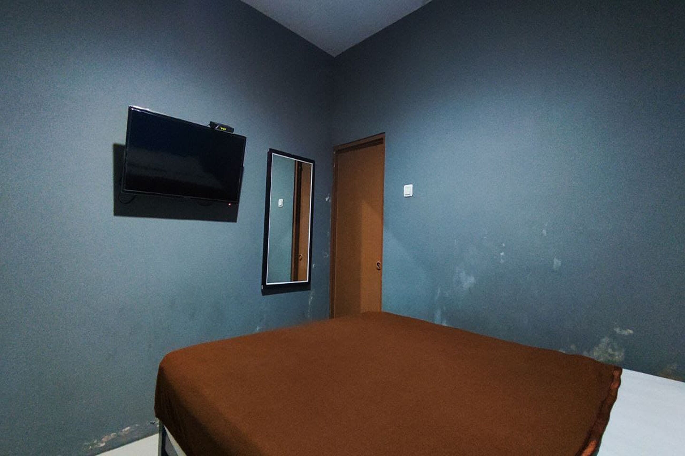 A room with a bed, a television mounted on the wall, and a door.