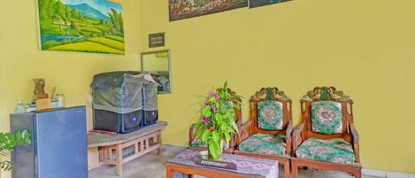 A living room with a reception desk, two wooden chairs, a coffee table, and a refrigerator.