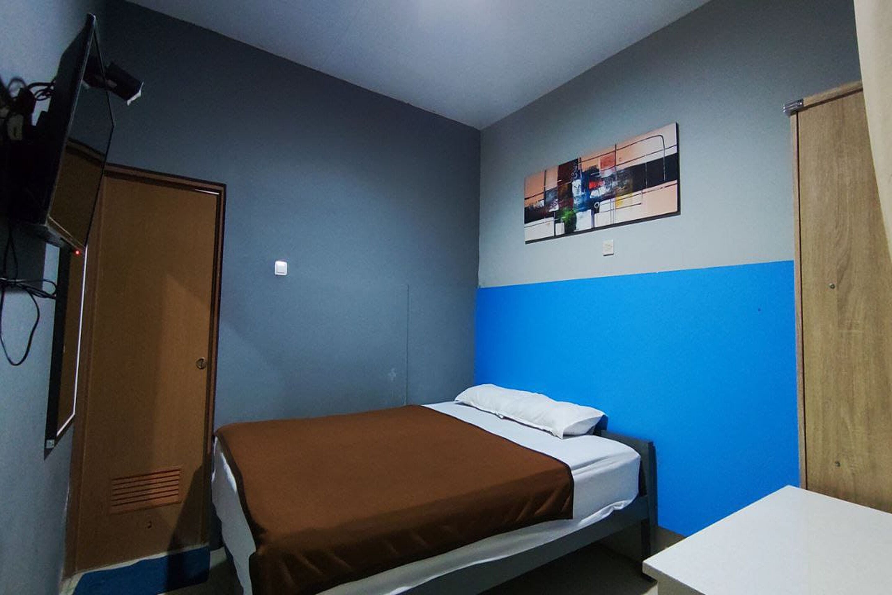 A bedroom with a bed, a desk, a wardrobe, and a painting on the wall.