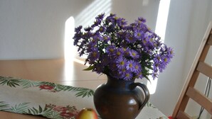 Een tafel met een Vogtland Journal tijdschrift, een vaas met paarse bloemen en een klein appel.