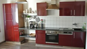 Een moderne keuken met rode keukenkastjes, een fornuis, oven en koffiezetapparaat.