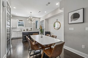 A modern kitchen with white cabinetry, a dining table with chairs, a pendant light, and a framed artwork on the wall. - Premium house for large groups with sky deck view! (Nashville)