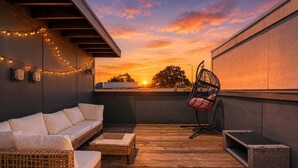 Eine Dachterrasse mit einer Couch, Korbstühlen und Lichterketten.