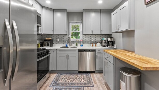 Una cucina moderna con mobili grigi, elettrodomestici in acciaio inossidabile, un piano di lavoro in legno e un tappeto decorato.