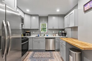 A modern kitchen with grey cabinets, stainless steel appliances, a wooden countertop, and a patterned rug. - Spacious Home in Troy (Troy)