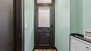 Un corridoio stretto con una porta di legno scura, un interruttore della luce e una piccola finestra con persiane.