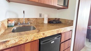 A kitchen with a granite countertop, stainless steel sink, wooden cabinets, and a black dishwasher. - Cozy Studio apartment in tranquil Cancún with AC (Cancún)