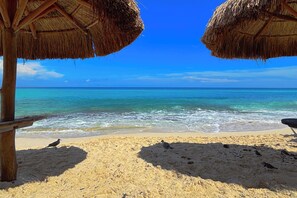 A beach with thatched umbrellas, clear blue water, and sandy shore. - Cozy Studio apartment in tranquil Cancún with AC (Cancún)