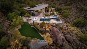 Une grande maison avec une piscine, entourée d’une pelouse bien entretenue et d’une végétation désertique.