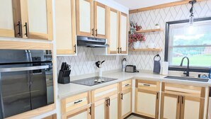 A modern kitchen with wooden cabinets, stainless steel appliances, and a window with a view of a tennis court. - Southern Magnolia 3BR/2Bath Home 5 min to base (Enterprise)