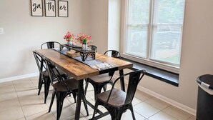 A dining area with a wooden table and black chairs, a vase with flowers, and a window with blinds. - Southern Magnolia 3BR/2Bath Home 5 min to base (Enterprise)