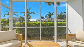 A room with two sofas and a round wooden table, large windows offering a view of palm trees and a house. - Beach Luxury Retreat • Walk to Beach & 5th Ave (Naples)
