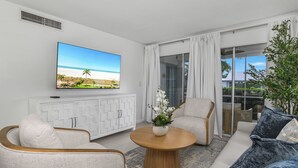 A modern living room with a flat-screen TV, white furniture, and a view of the outdoors. - Beach Luxury Retreat • Walk to Beach & 5th Ave (Naples)