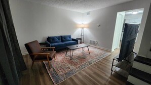 A living room with a blue sofa, a brown armchair, a coffee table, and a floor lamp. - King Bed| Pet Friendly |2BR Townhome with Parking (Louisville)