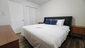 A bedroom with a bed, a wooden nightstand, a wooden dresser, and white double doors. - King Bed| Pet Friendly |2BR Townhome with Parking (Louisville)